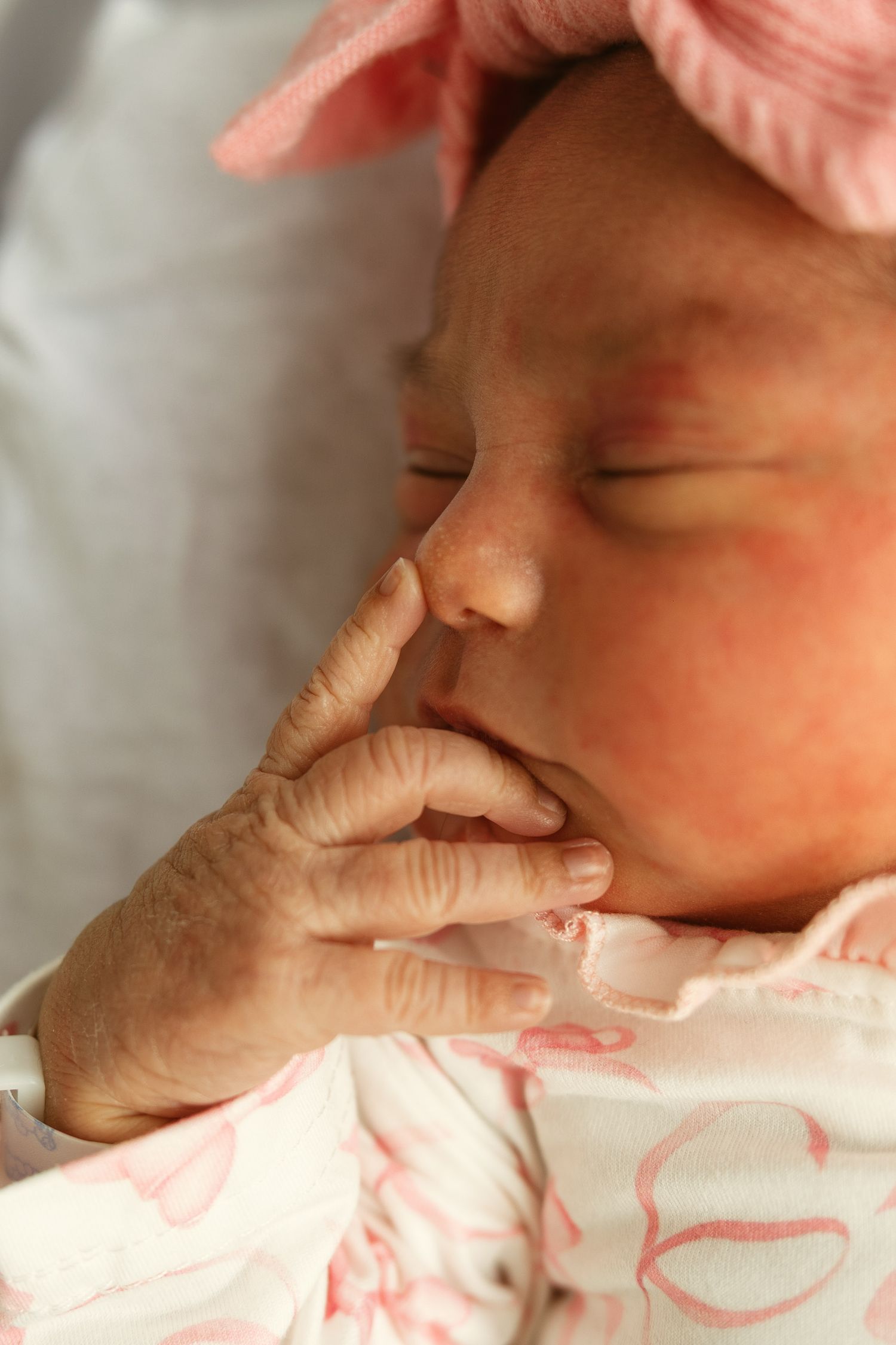 Newborn baby girl sleeping peacefully with hand near face, wearing pink bow headband and floral outfit.