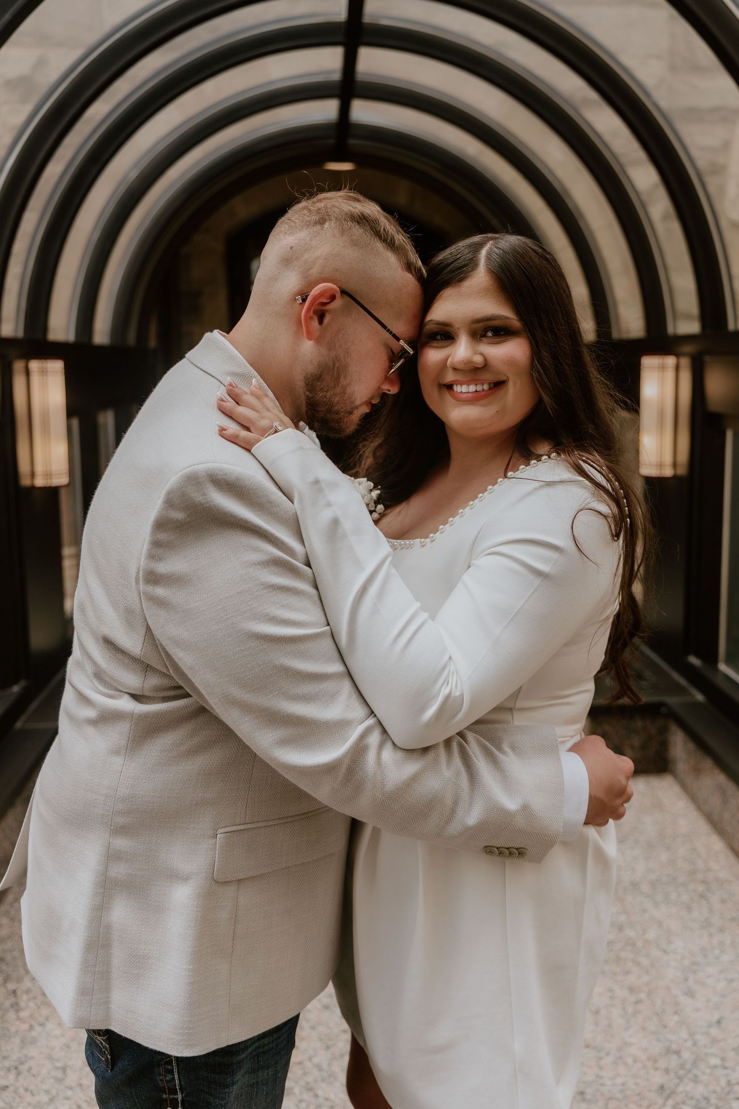 Romantic moment captured under an arched hallway with couple in coordinating white outfits.