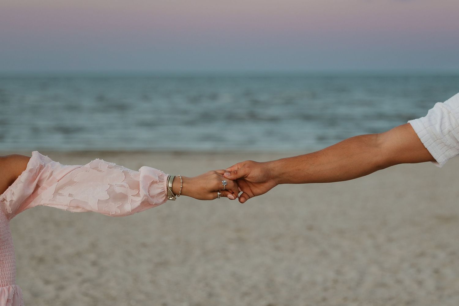 Close-up of hands holding each other while walking on a beach during sunset.