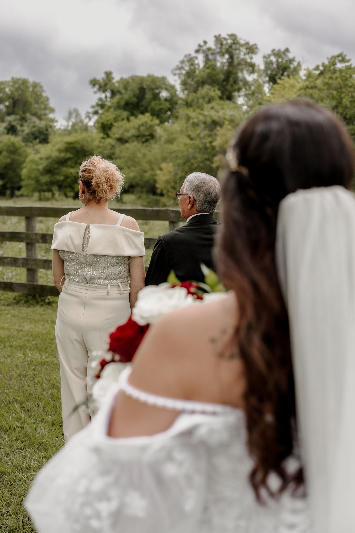 Wedding party walking across a grassy field with wooden fence in background.