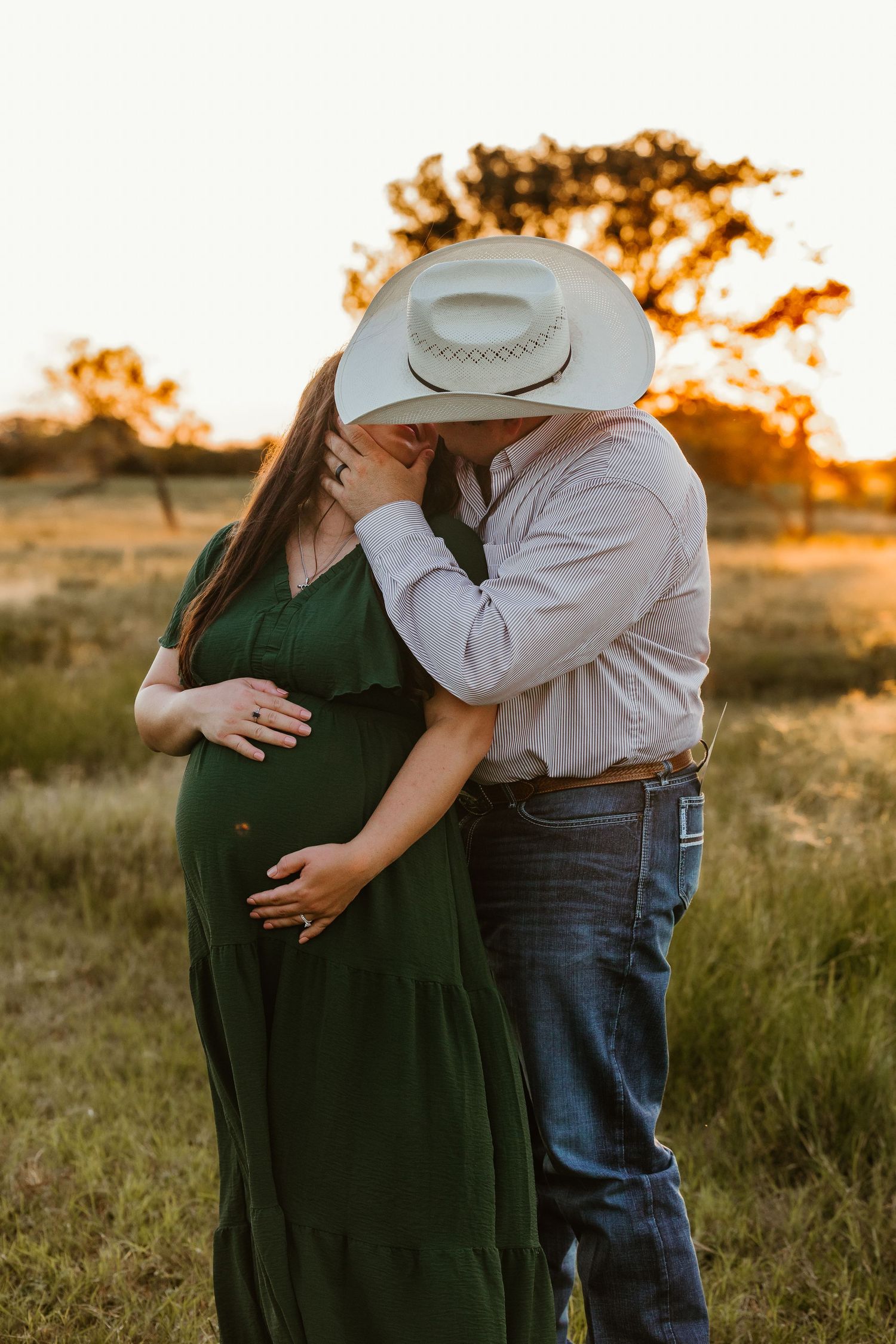 Couple embracing in field at sunset wearing western attire in Goliad, TX.