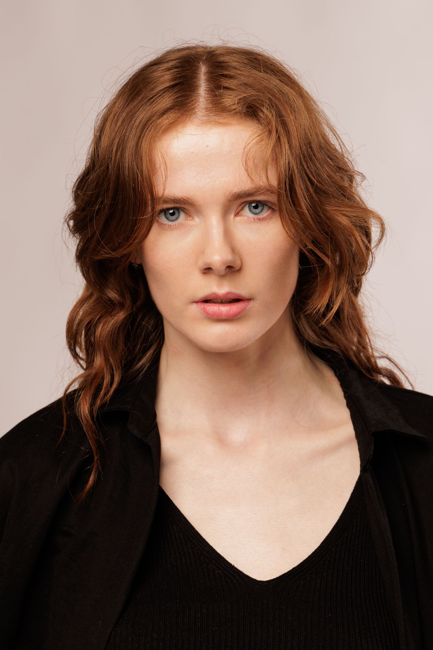 A portrait photo featuring striking blue eyes, wavy auburn hair, and a black top against a neutral background.