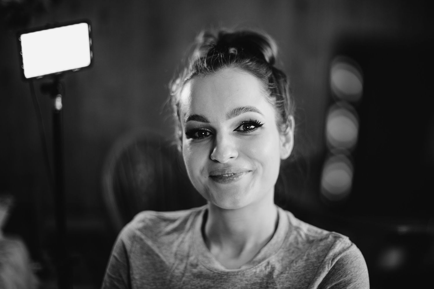A black and white portrait shows a woman wearing a gray sweater smiling warmly at the camera.