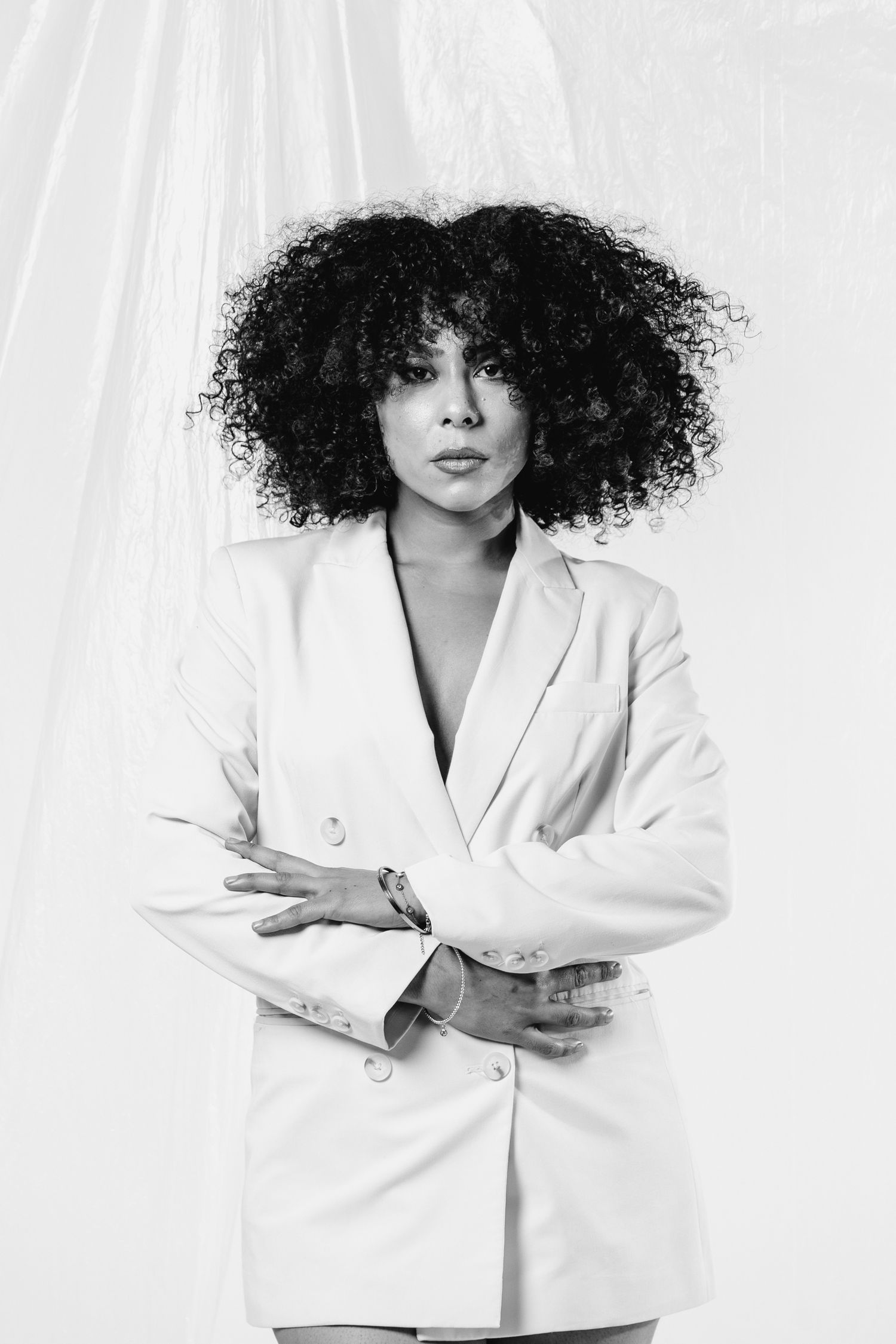 Black and white portrait of a person with voluminous curly natural hair wearing a white blazer against a light backdrop.