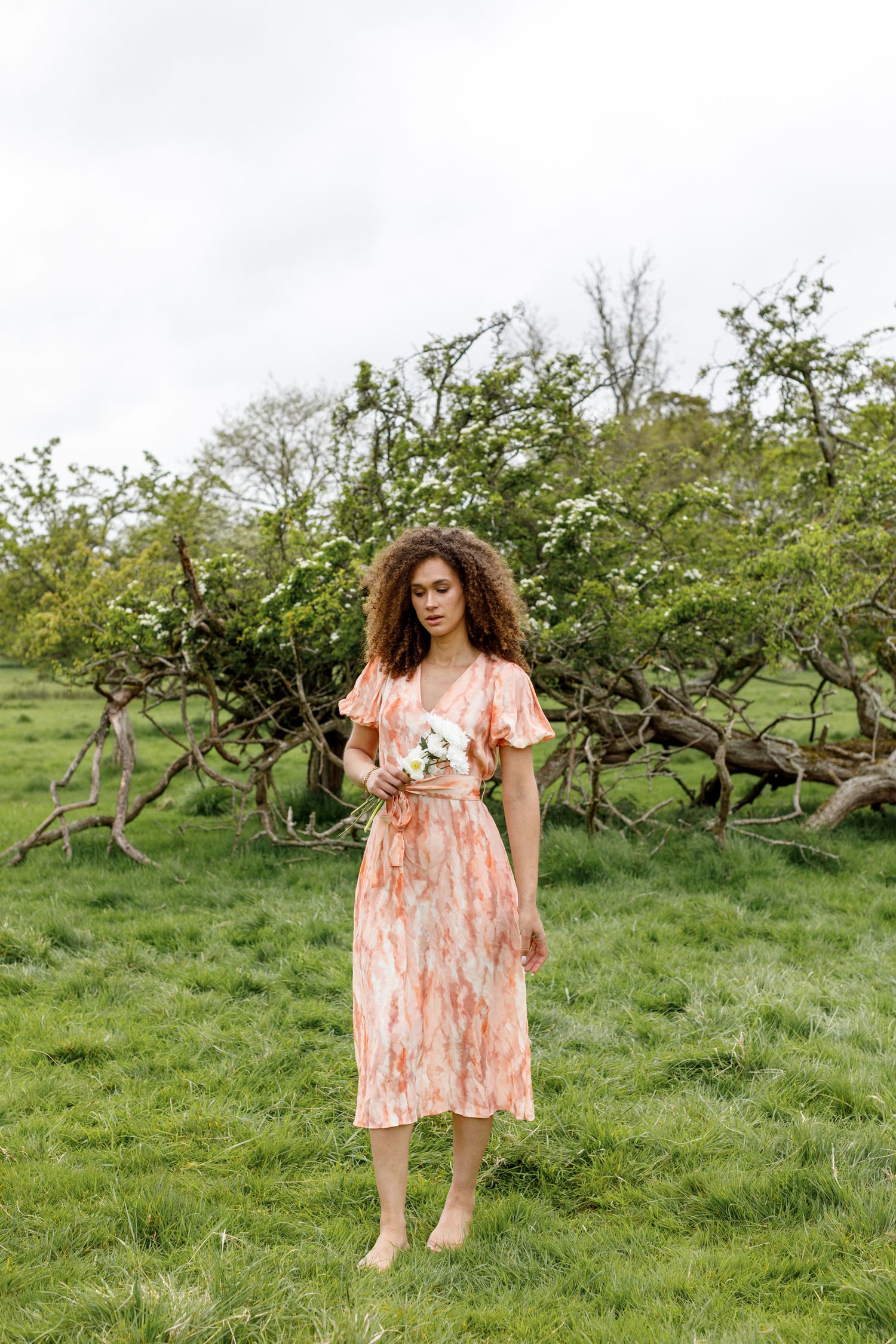 A flowing peach-colored spring dress with flutter sleeves stands out against lush green garden backdrop.