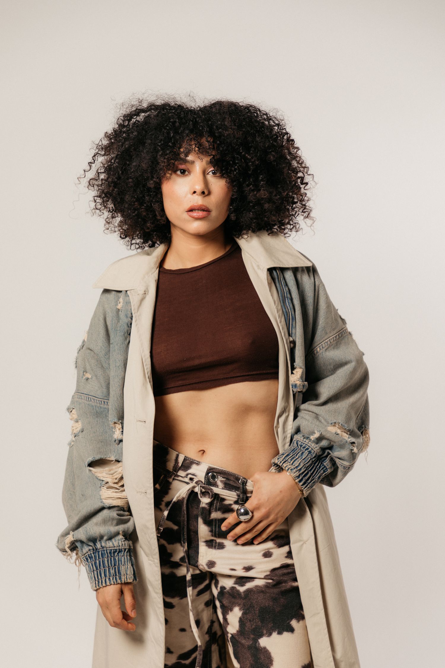 Stylish model wearing brown crop top, tie-dye pants and beige oversized jacket poses against neutral background.
