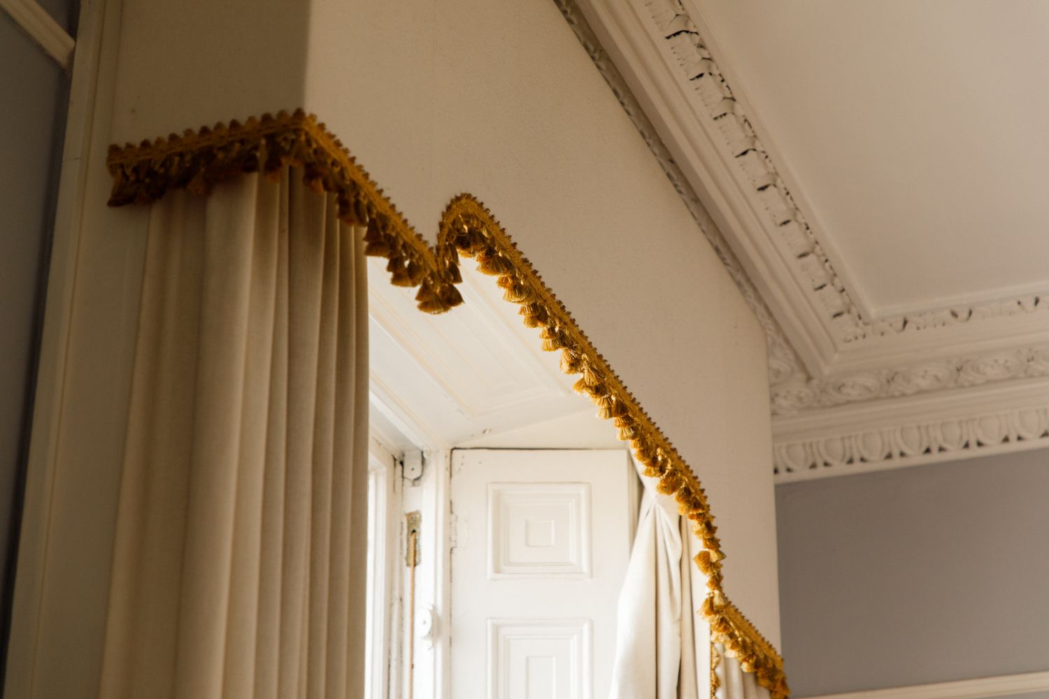 Gold metallic tinsel garland decoratively drapes along the crown molding and doorway of an elegant white room.