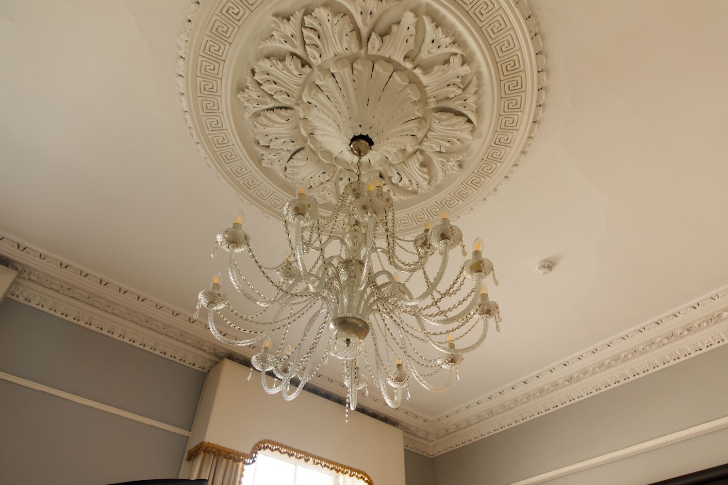 An elegant crystal chandelier hangs from an ornate ceiling medallion with detailed Victorian-style plasterwork molding.