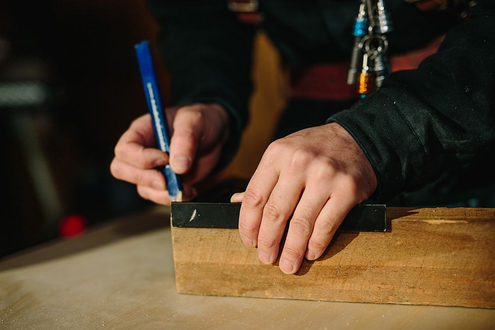 Close-up of hands marking measurements on wooden surface with blue pencil.