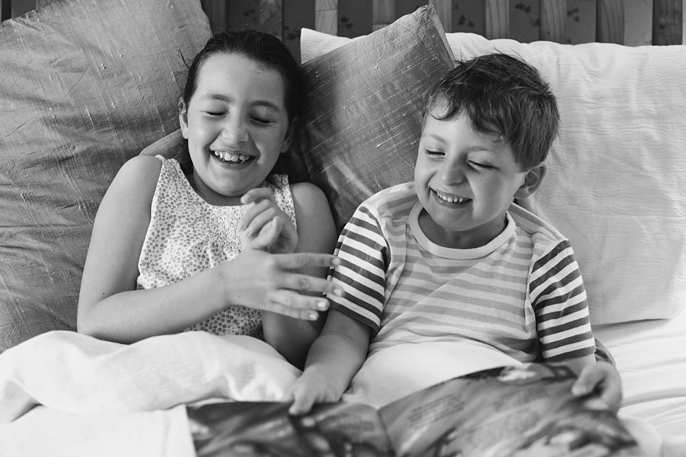 Children laugh together while relaxing on white bedding.