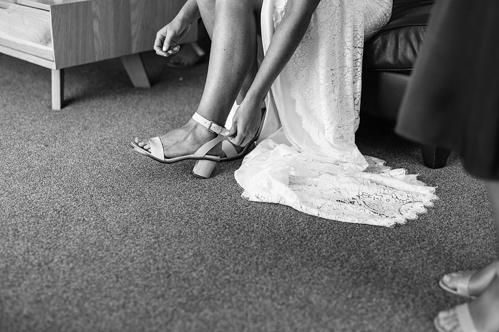 Close-up details of wedding dress hem and shoes on grey carpet.
