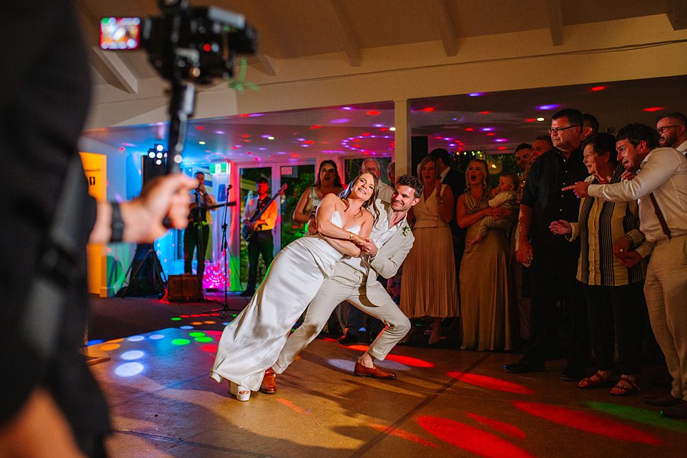 Wedding reception dance floor with colorful lighting and guests celebrating in a rustic venue.
