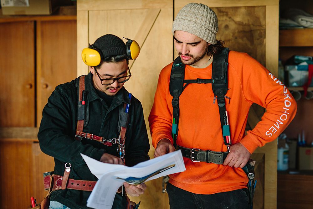 Two workers in protective gear review documents together in workshop.