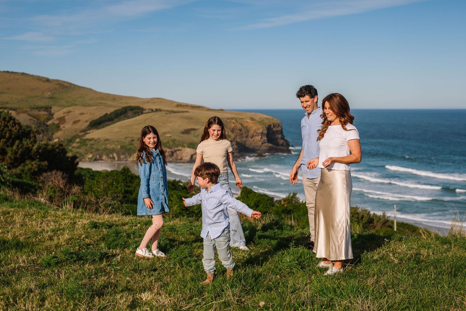 A couple and their toddler walk along the scenic coastal cliffs overlooking the Pacific Ocean on a sunny day.
