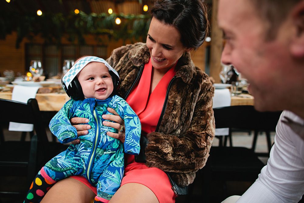 A candid moment at an outdoor reception with a baby wearing a blue snowsuit.
