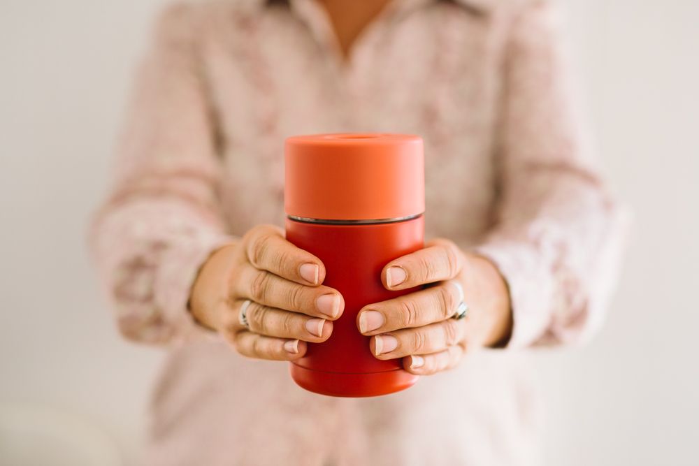 Hands holding a bright orange and red cylindrical container against light background.