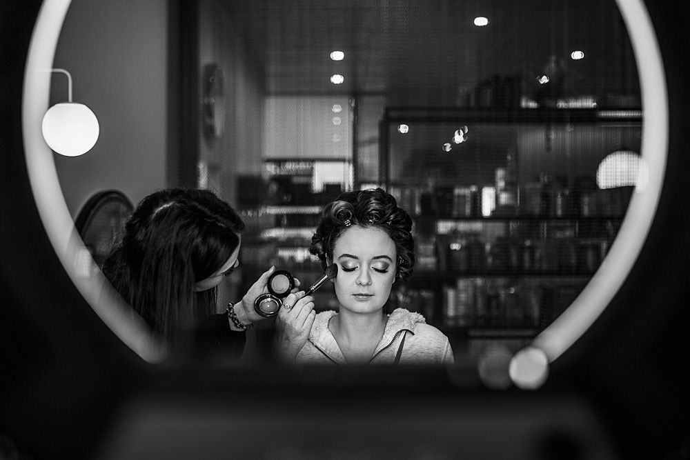 A reflection in a circular mirror shows wedding day makeup preparations in progress.