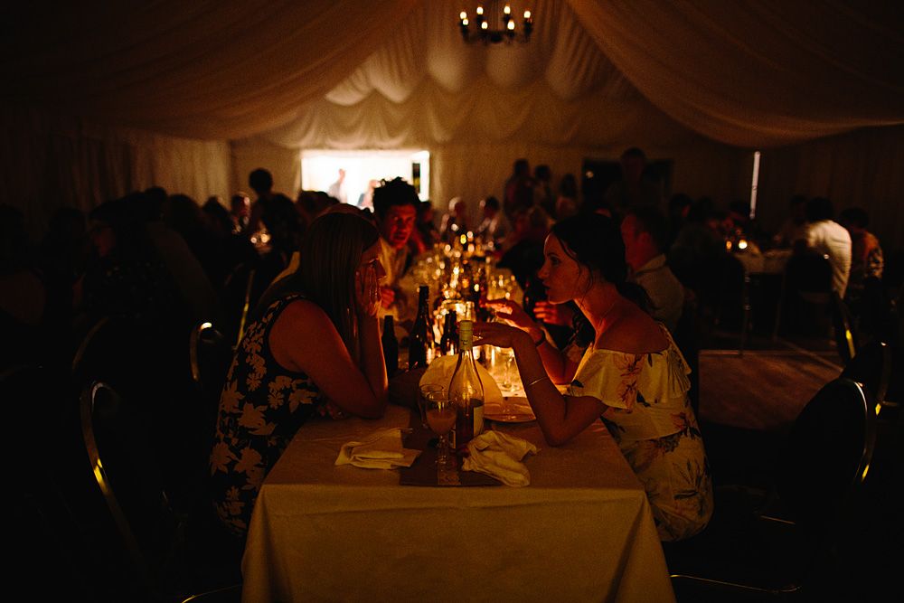 Wedding reception guests dine at candlelit tables under elegant draped tent lighting.