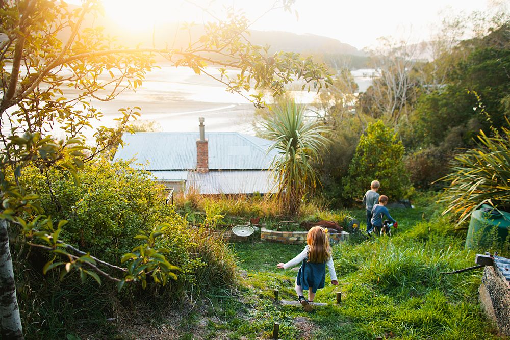 People walking down a lush green coastal path at sunset with a lighthouse visible in the distance over the water.