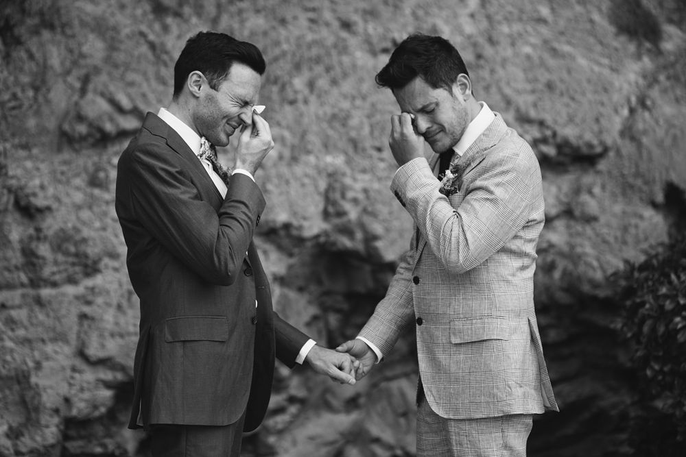 Couple sharing intimate moments against rocky cliff backdrop in black and white.