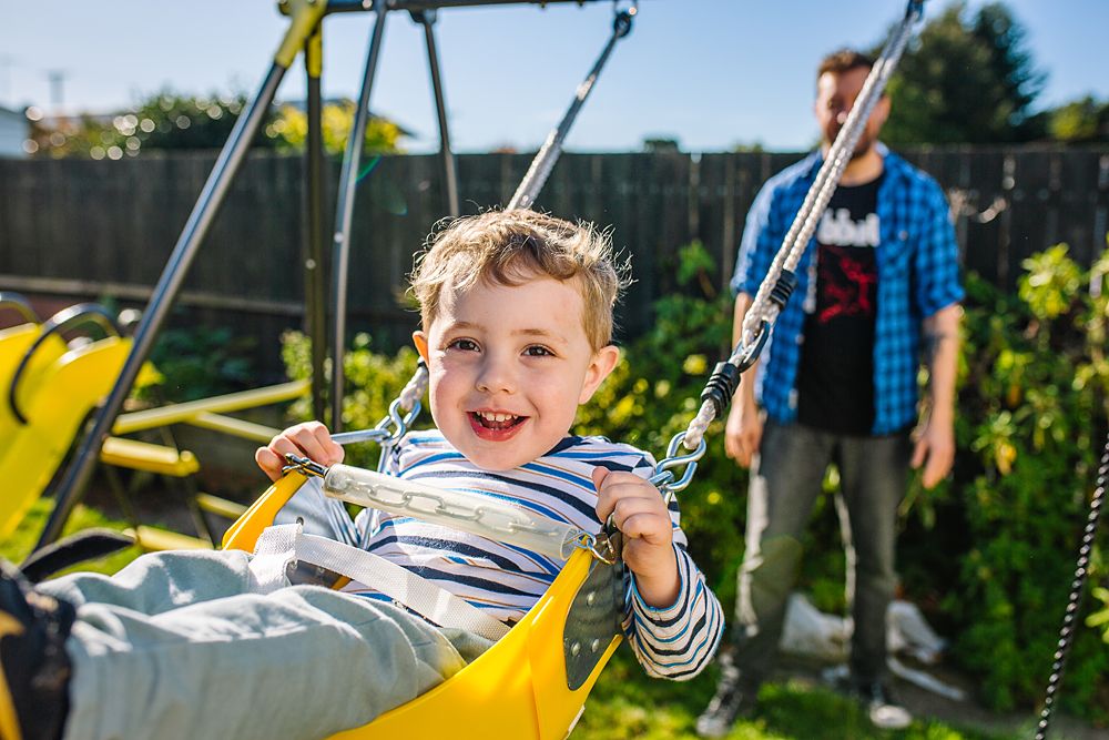 Children playing and swinging on yellow playground equipment on a bright sunny day.