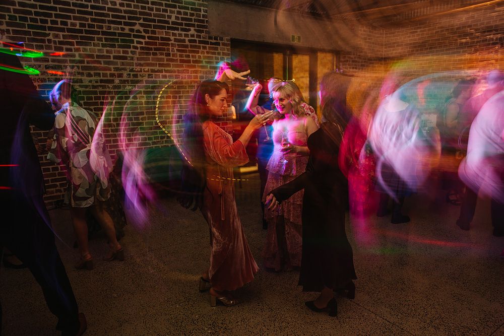 People dancing at a party with colorful motion-blur light effects against brick walls.