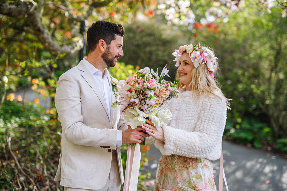 Couple poses in a garden setting surrounded by blooming flowers and greenery.