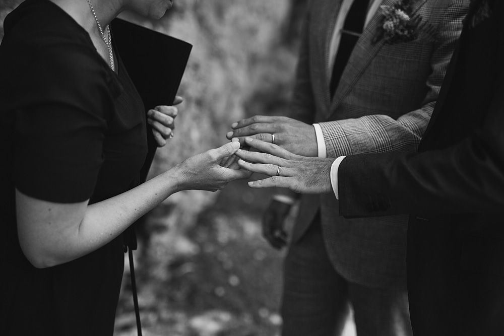 A black and white close-up shot of hands exchanging rings during a wedding ceremony.