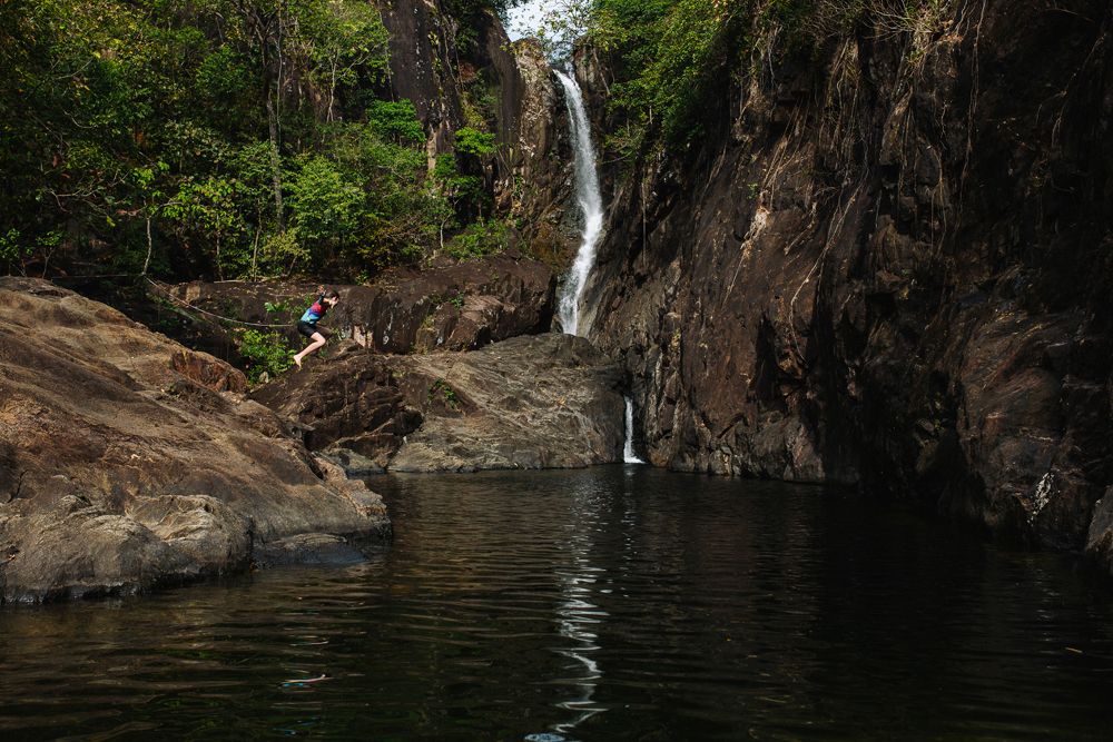 Scenic waterfall cascading down rocky cliffs into a serene swimming hole surrounded by lush forest.