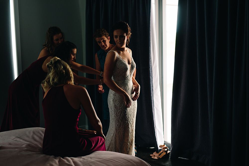 A wedding dress fitting session in a dimly lit room with dramatic window lighting.
