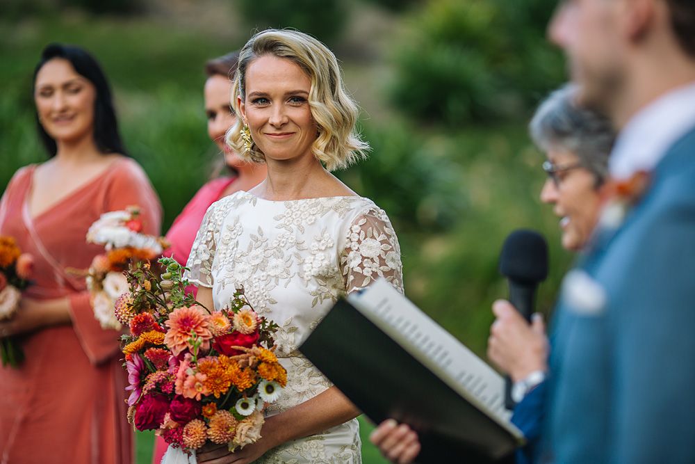 Wedding party members hold vibrant autumn bouquets with orange and red flowers against an outdoor backdrop.