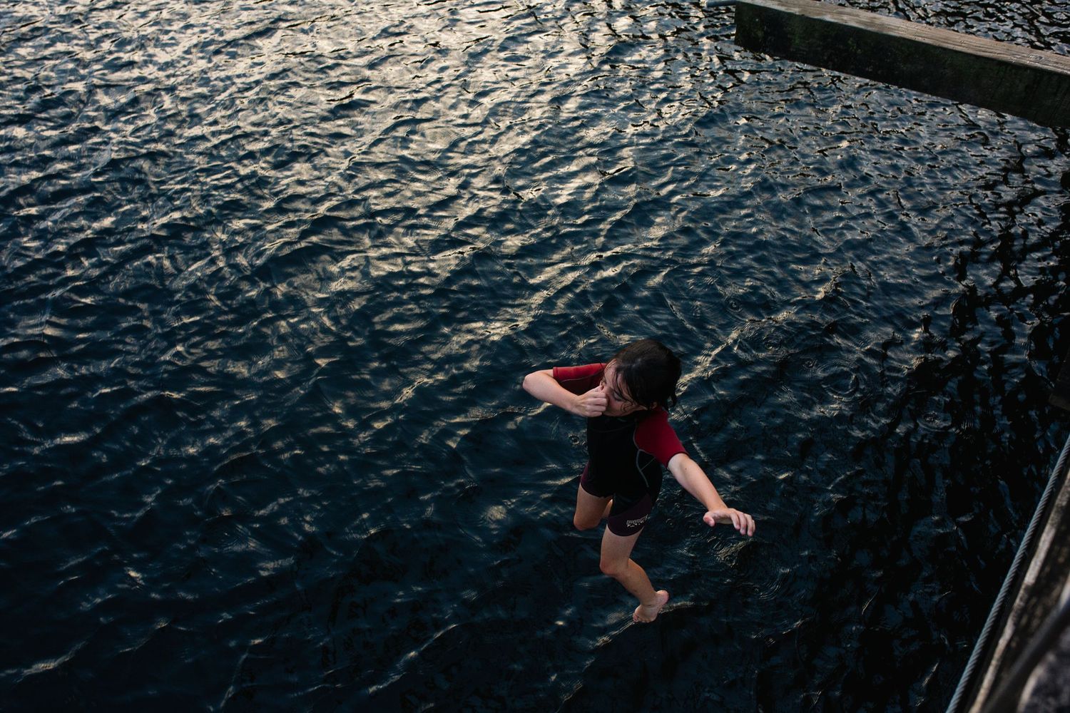 A sequence of diving action shots showing a person performing a backflip into dark rippling water at dusk.