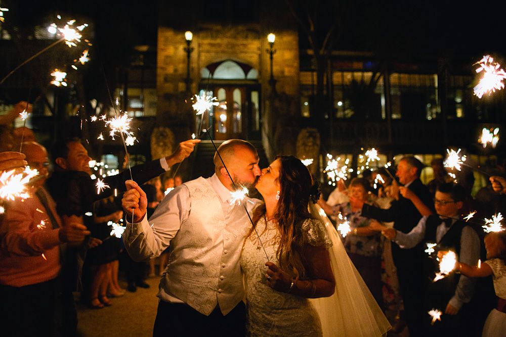 Wedding guests hold sparklers creating a magical nighttime atmosphere outside a grand building.