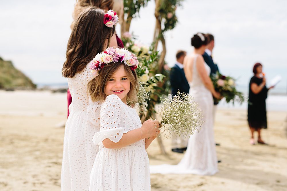 A beach wedding scene with a young attendant in white dress and flower crown.