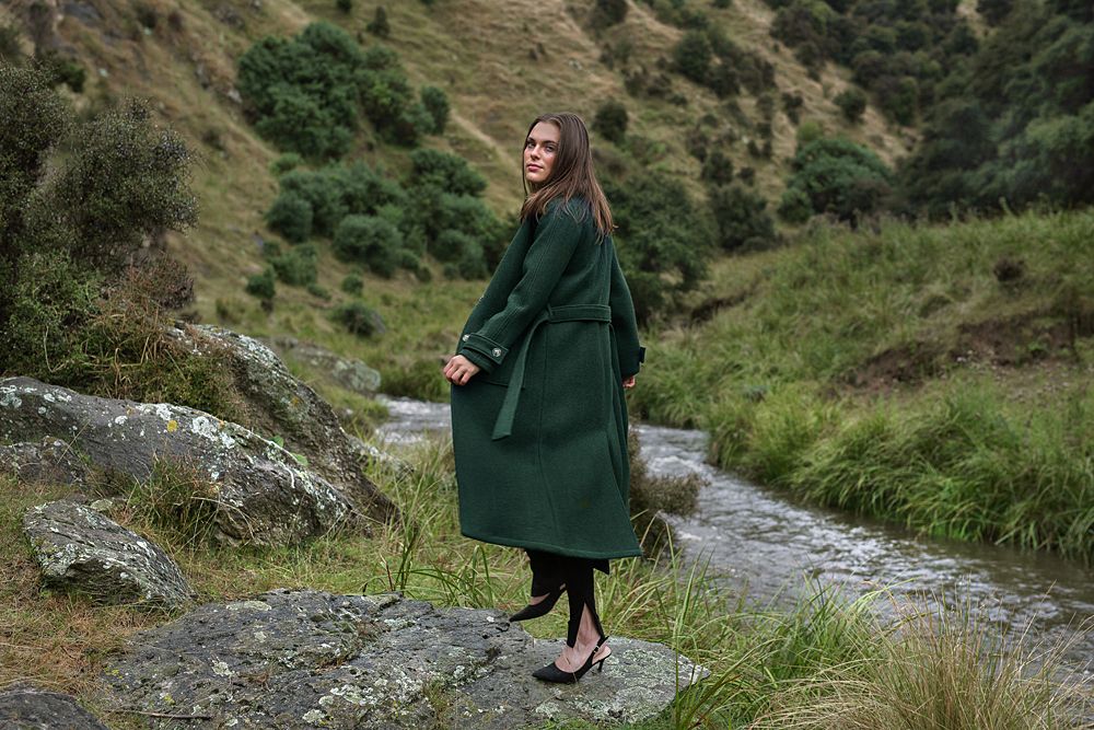 Person in green coat walking along scenic mountain trail with grassy slopes.