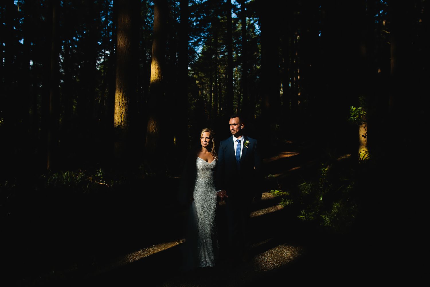 A dramatic forest wedding portrait with sunlight filtering through dark trees.