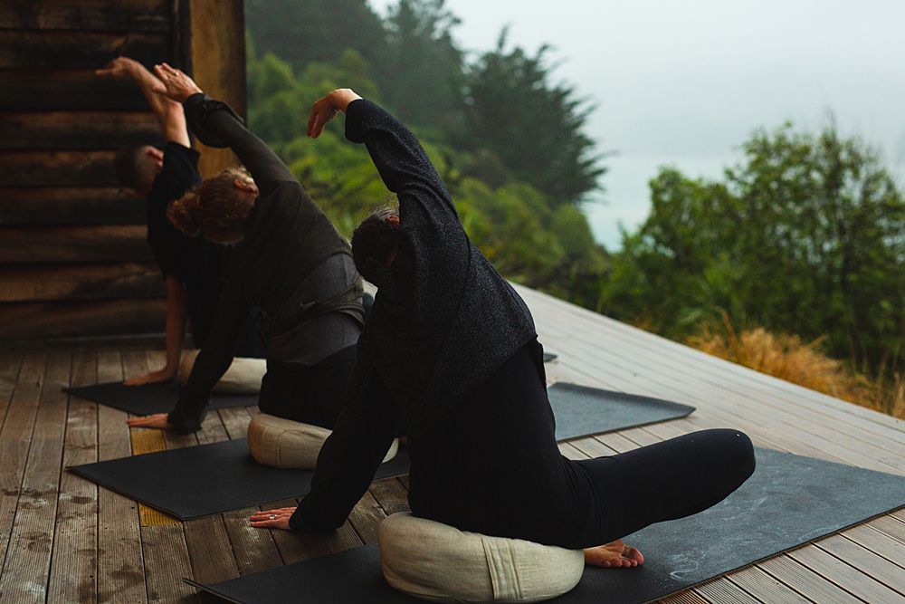 Group practicing yoga poses on outdoor deck surrounded by misty forest scenery.