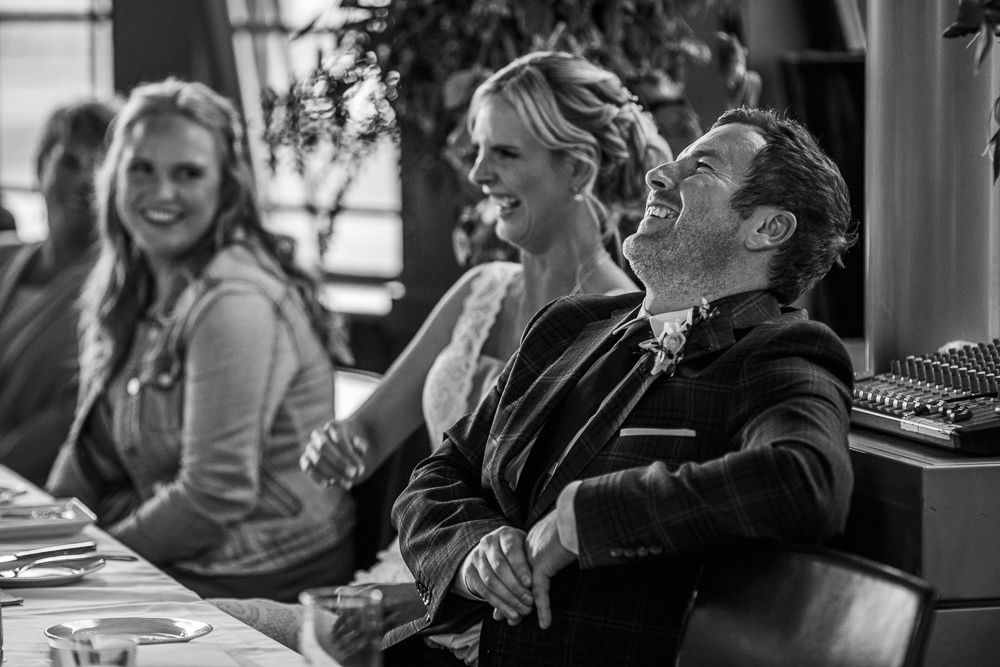 Wedding guests share a candid moment of laughter in black and white photography.