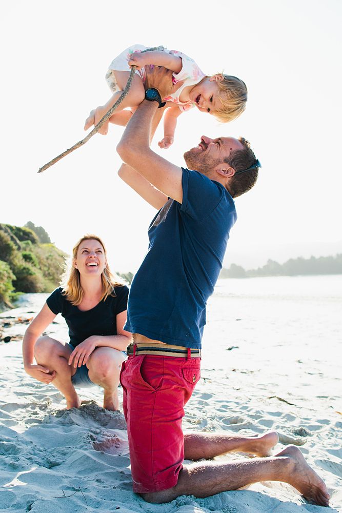 Playful family moment at the beach with laughter and lifting against the golden sunlight.