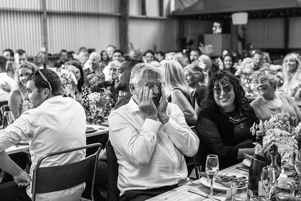 Black and white photo of wedding reception guests showing emotional reactions at dining tables.