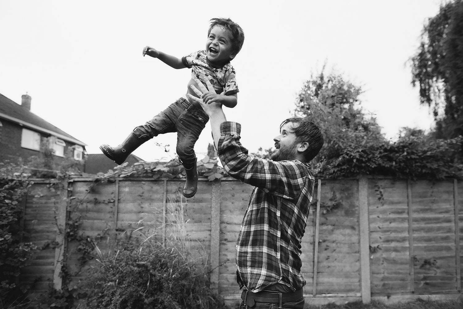 Person jumping and playing outdoors near a wooden fence in a backyard setting.