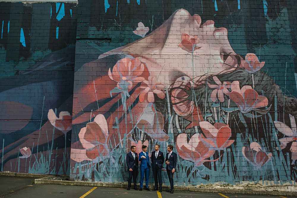 Large floral mural painted on brick wall serves as wedding photo backdrop.
