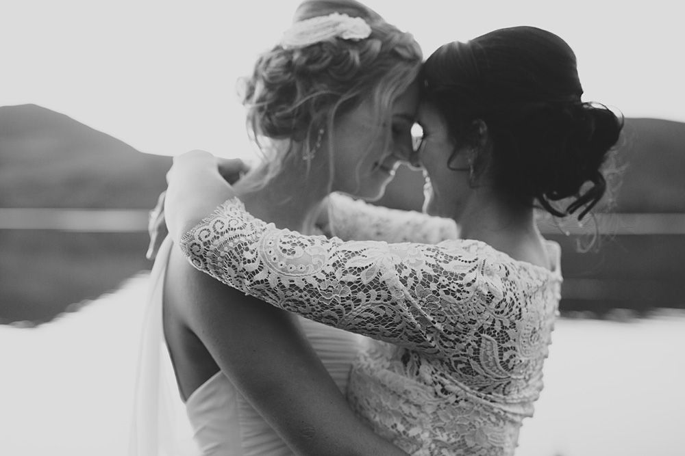 Two people in wedding attire embrace in an intimate black and white silhouette against mountains.