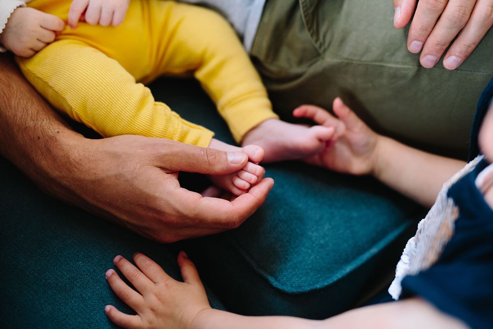 Baby wearing yellow pants being held on a cozy couch.