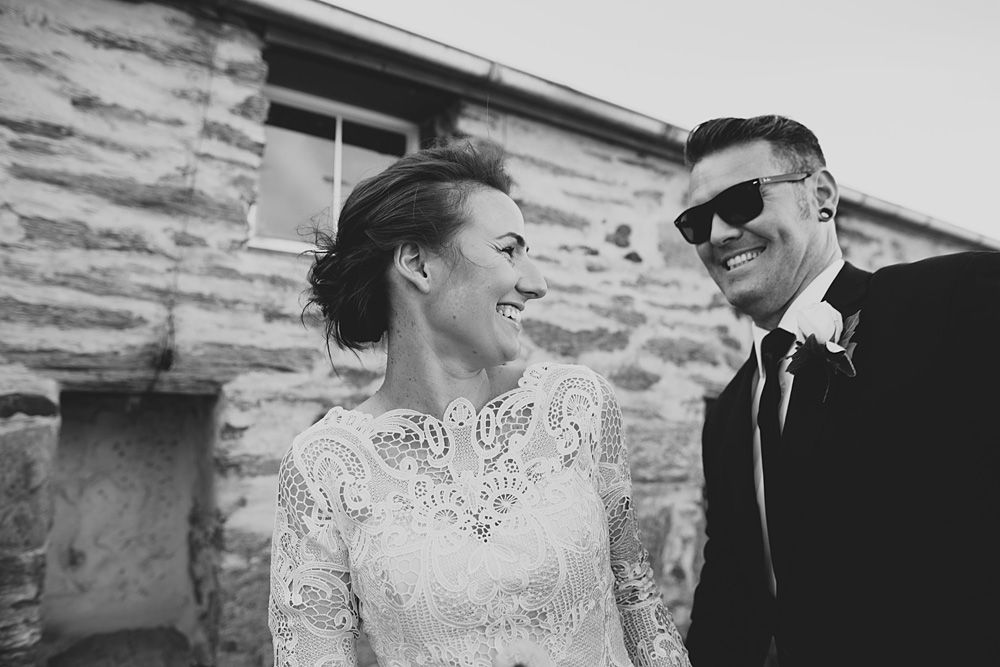 Black and white photo of a couple on their wedding day, with the bride in lace and groom wearing sunglasses.
