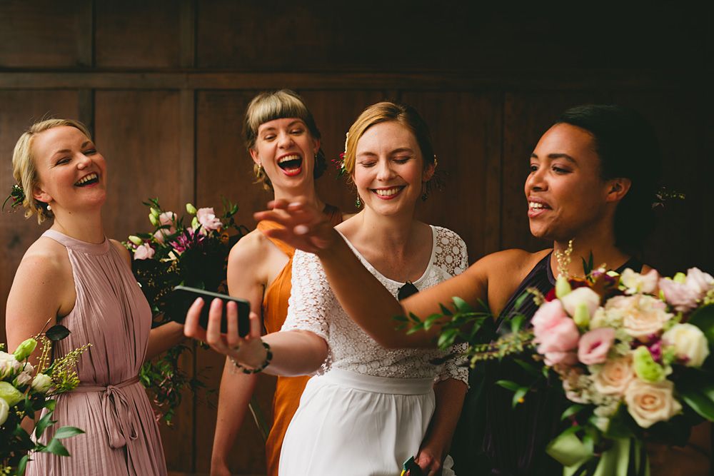 Wedding party members laugh together while holding beautiful floral bouquets.