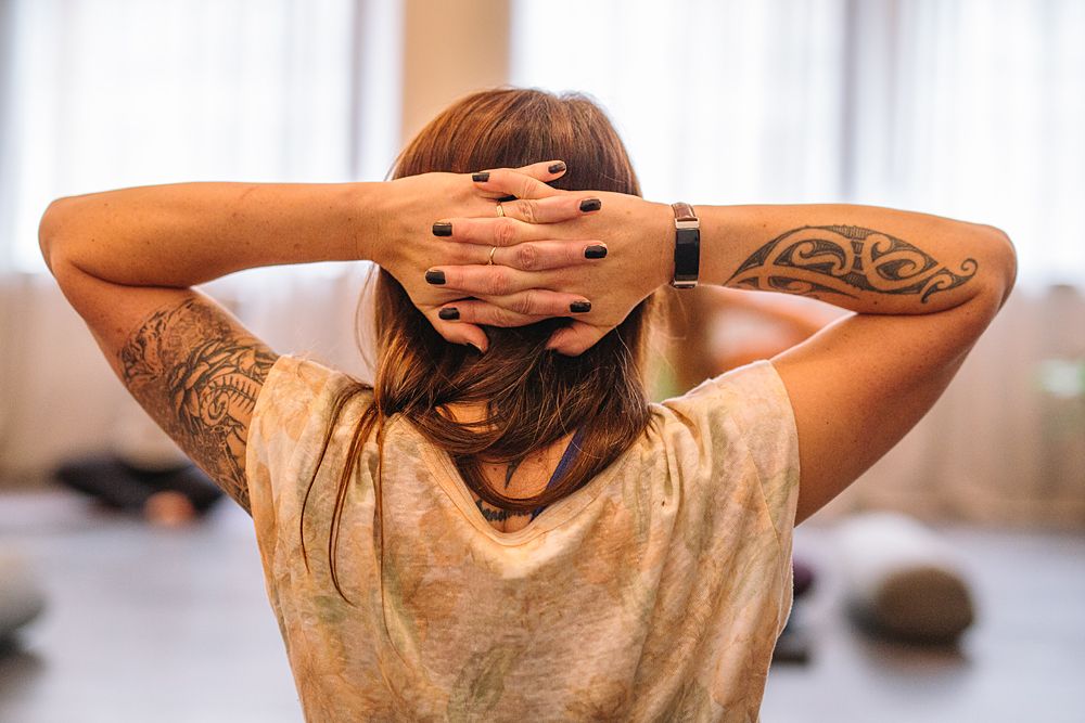 Person with tattoo stretching in sunlit room with wooden floors.