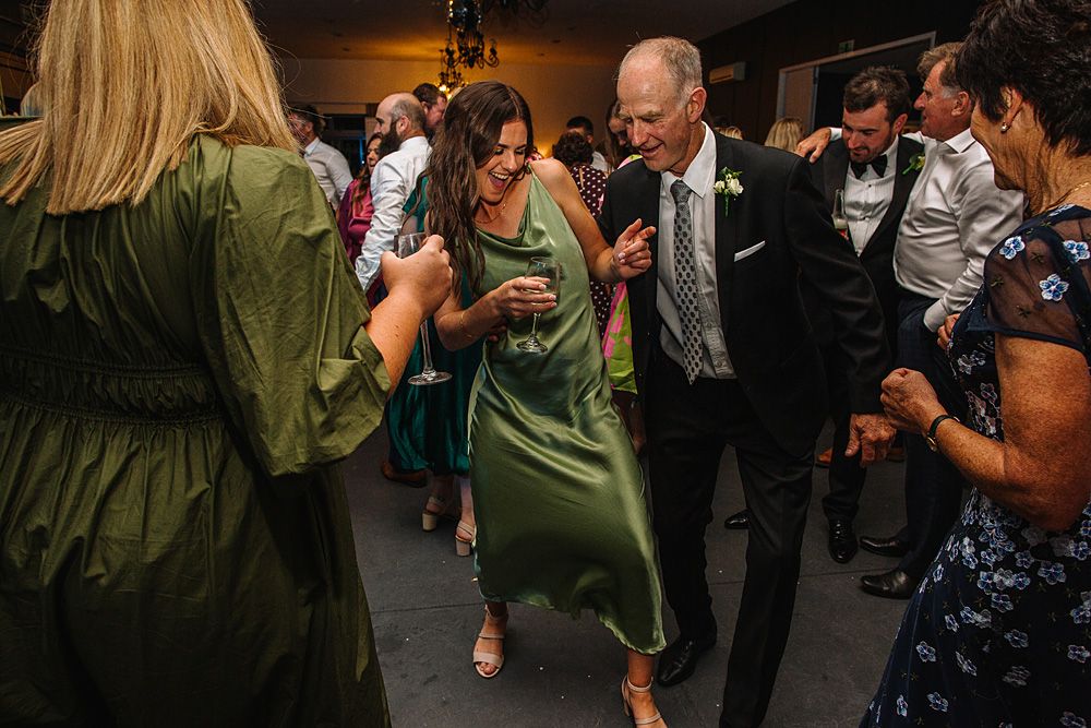 Reception guests dancing in formal attire under atmospheric venue lighting.