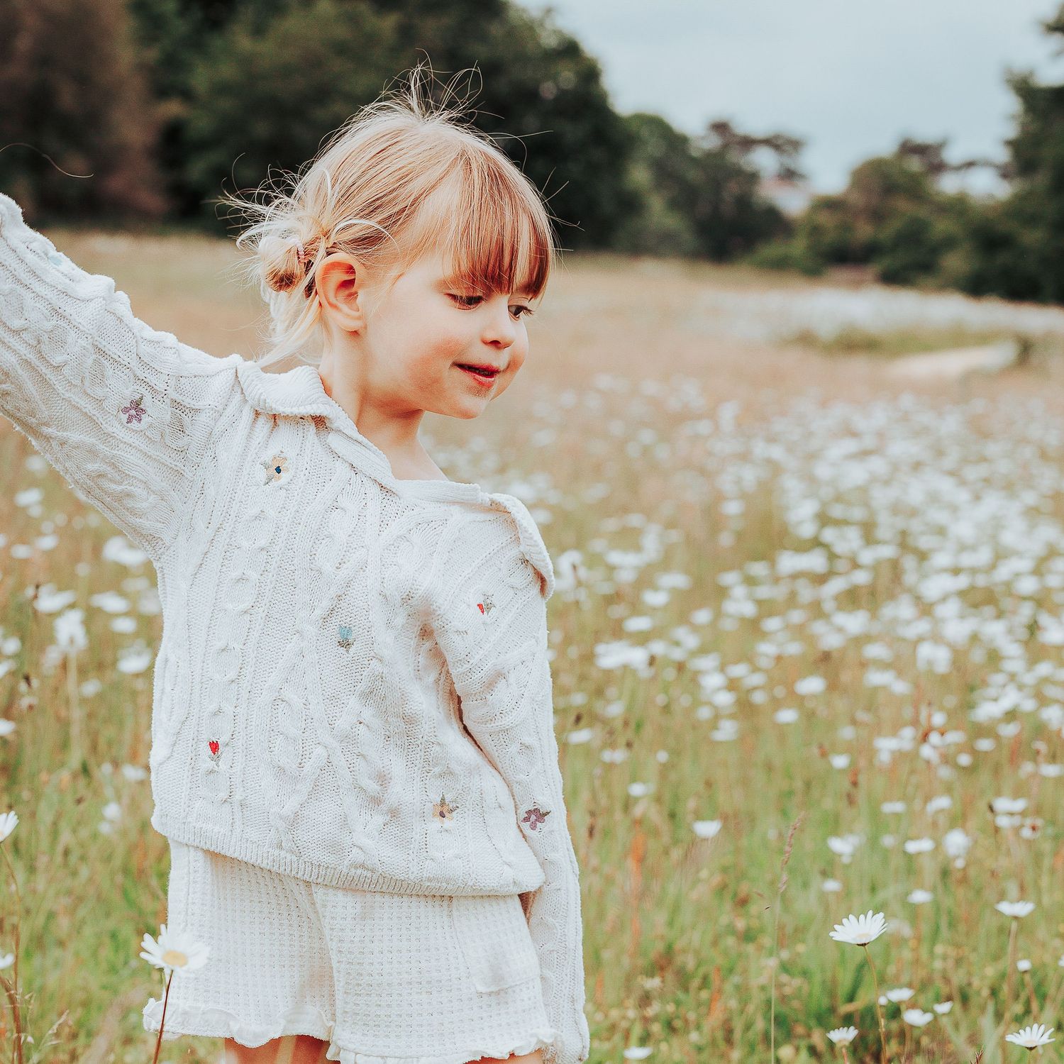 Natural preschool photography  showing happy child in a nursery garden playing in some oxeye daisies.