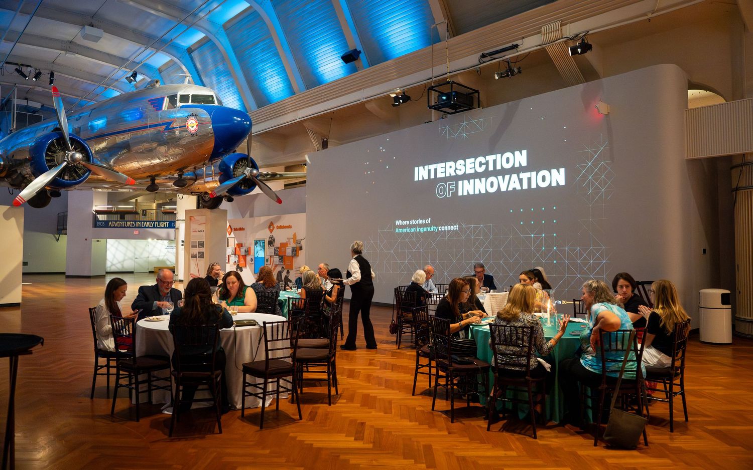 Corporate event space with blue uplighting and 'Intersection of Innovation' projection on wall.